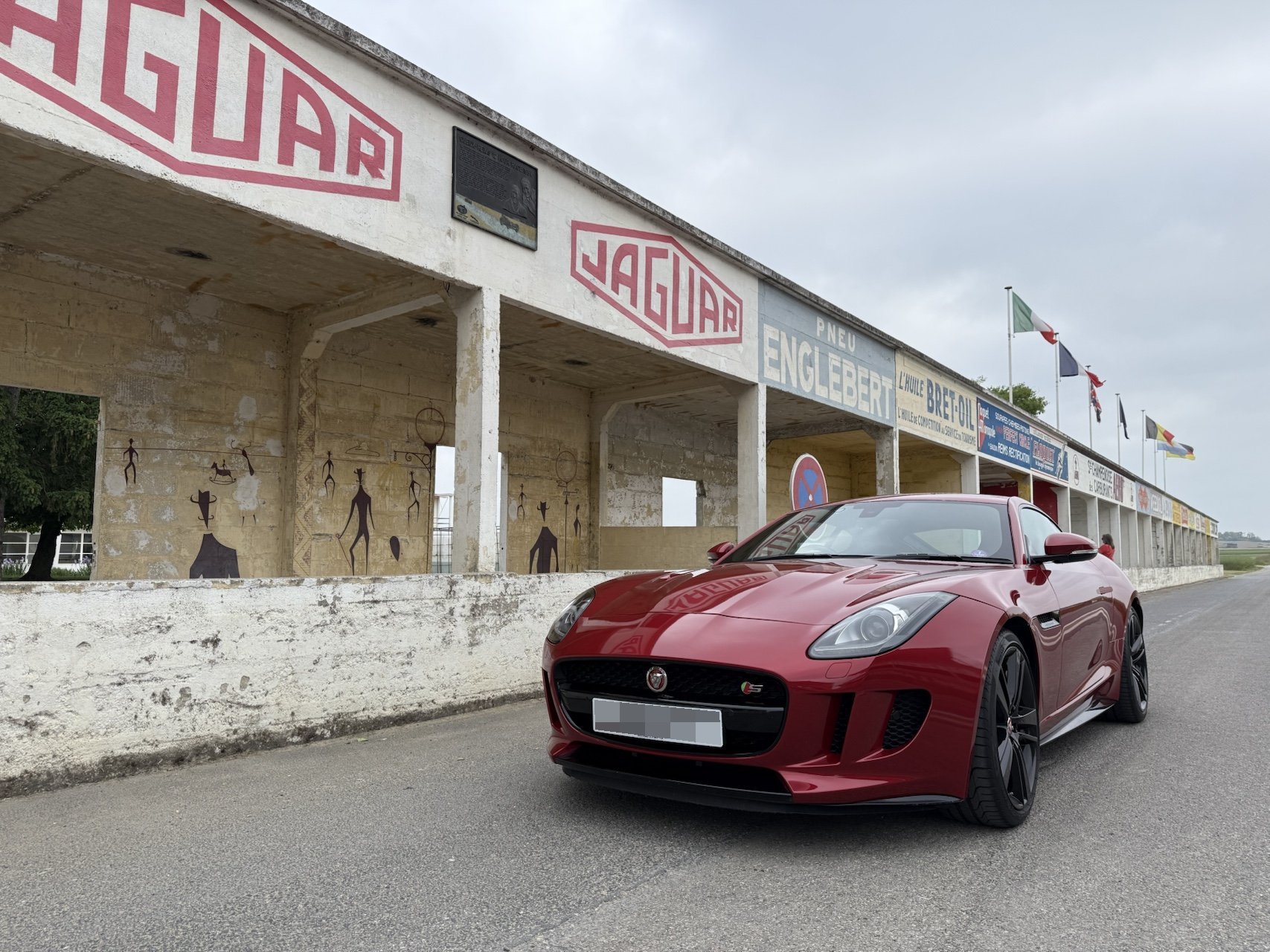 A red Jaguar F-Type in front of the vintage Jaguar pit signage at a historic racing circuit