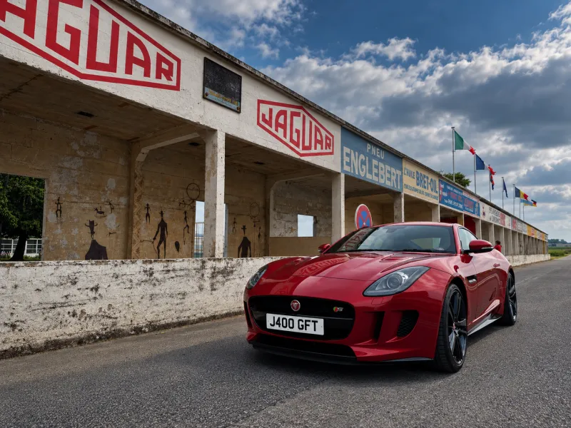 A red Jaguar F-Type in front of the vintage Jaguar pit signage at a historic racing circuit